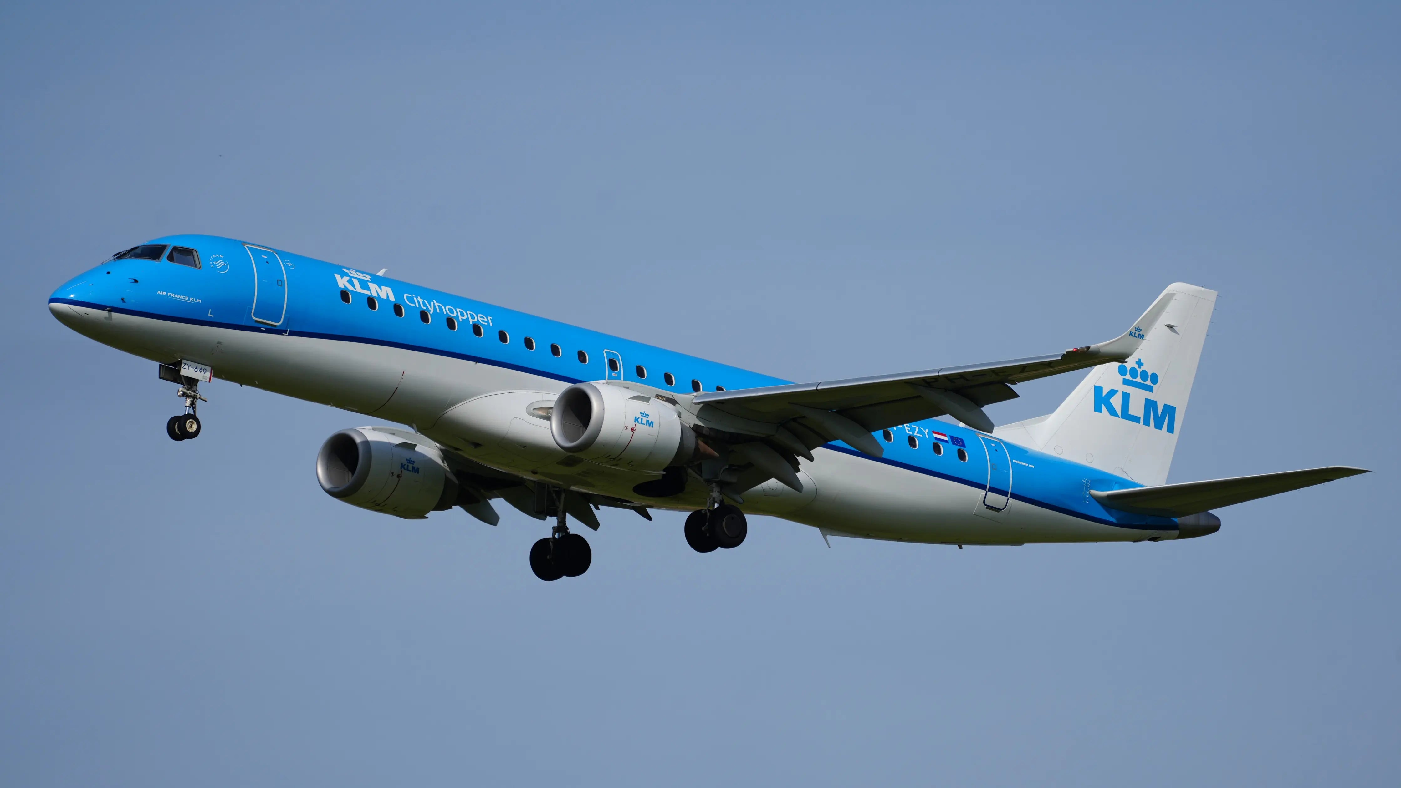 KLM Cityhopper Embraer ERJ-190STD aircraft in flight against a clear blue sky.