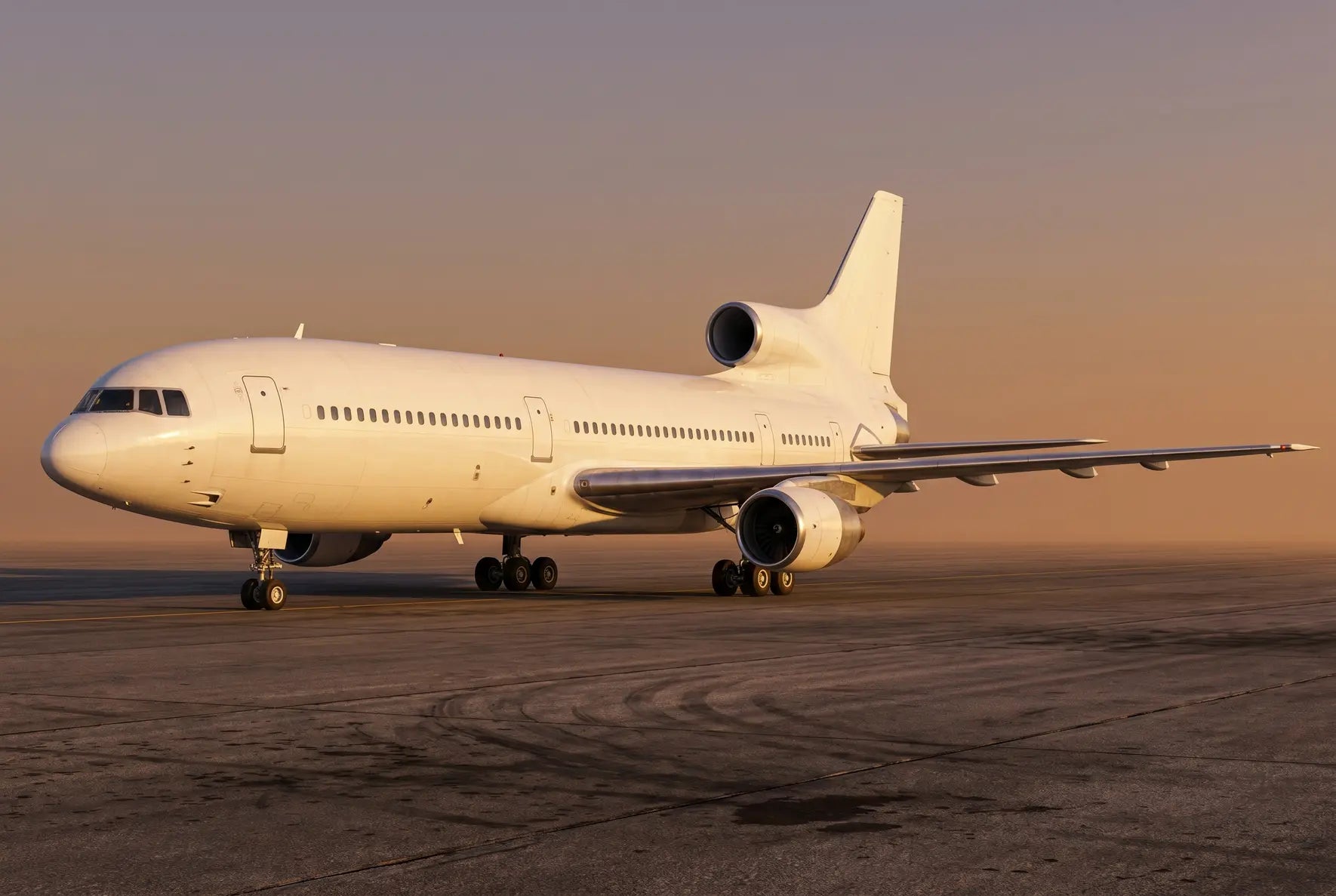 Lockheed L-1011-250 aircraft parked on an airport tarmac at sunset, showcasing its distinctive trijet design and sleek fuselage.