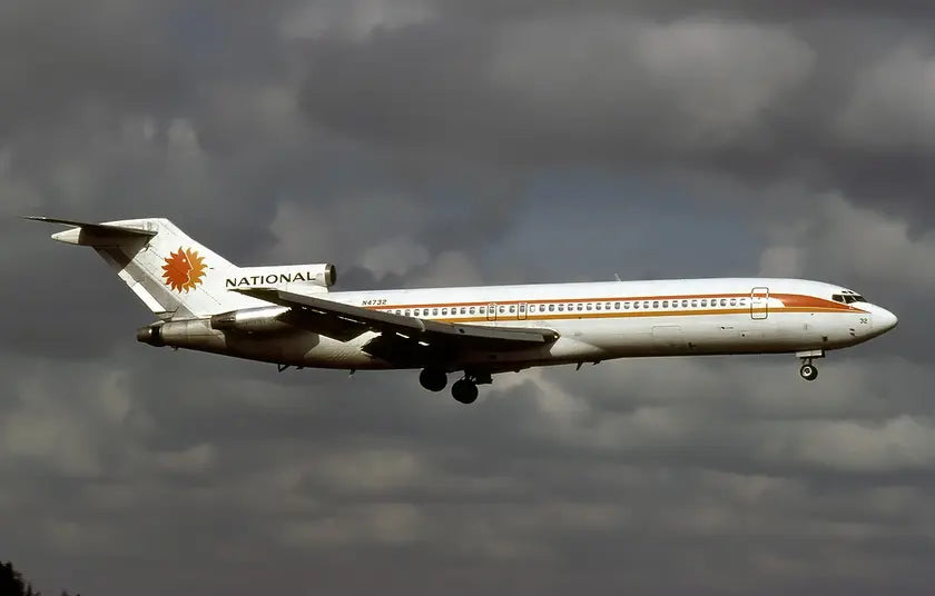 A Boeing 727-235 airplane of National Airlines in flight against a cloudy sky, showing its side with a distinctive orange sun logo on the tail.