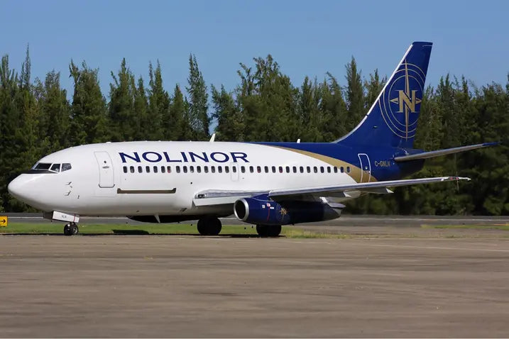 A Nolinor Aviation Boeing 737-200 aircraft parked on a runway with trees in the background.