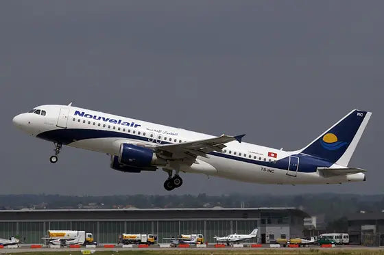 Nouvelair Airbus A320 aircraft, registration TS-INC, taking off from a runway with overcast sky in the background at an airport.