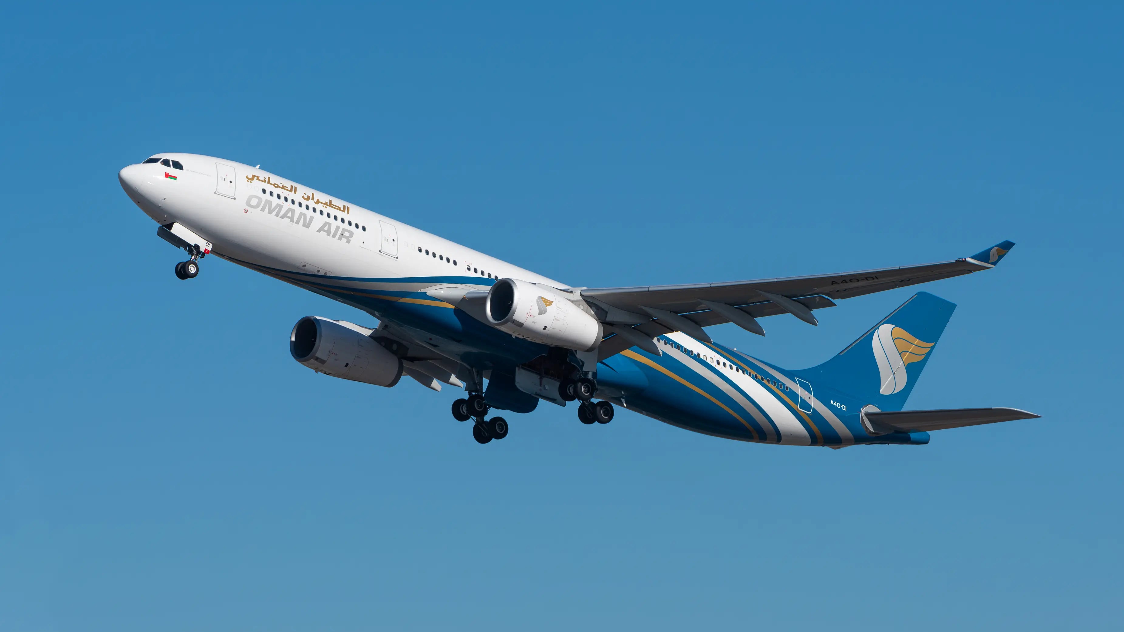Oman Air Airbus A330-343 in flight with undercarriage extended against a clear blue sky.