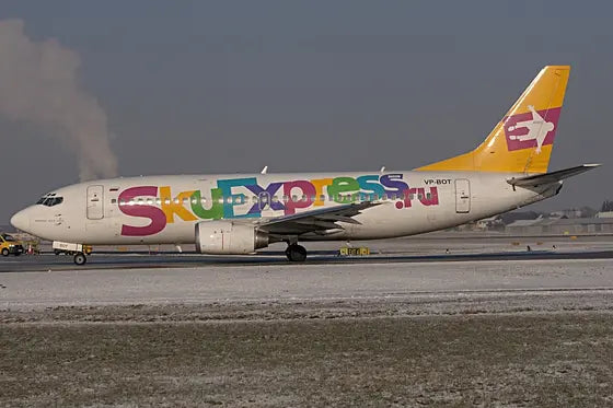 Sky Express Boeing 737-300 VP-BOT airplane on a snowy runway with colorful logo on fuselage, yellow tail fin, and visible airport background.