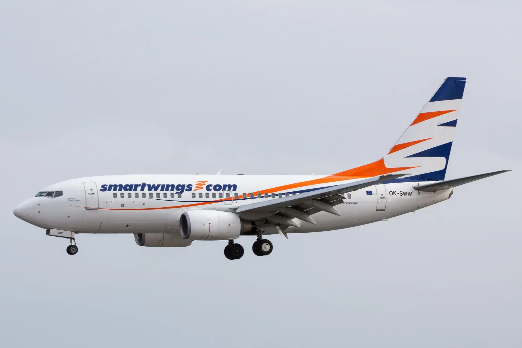 Smartwings Boeing 737 aircraft in flight with visible landing gear, white fuselage, and orange and blue stripes on the tail.