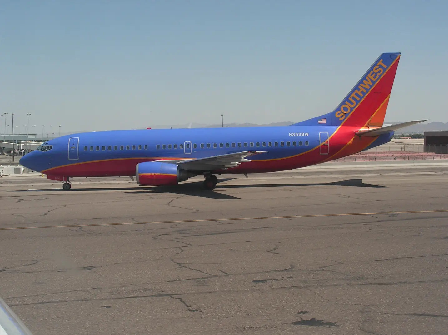 A Southwest Airlines plane with blue and red livery is parked on the tarmac at an airport, with mountains visible in the distance.