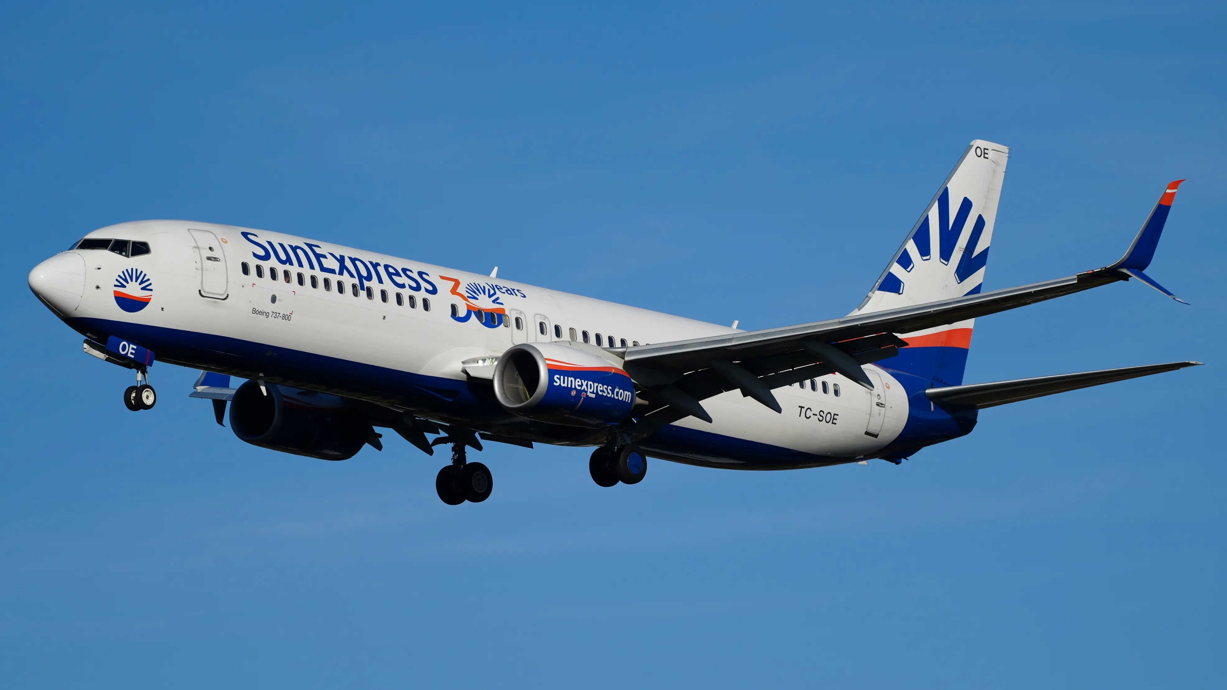 SunExpress Boeing 737-8HC(WL) aircraft TC-SOE in flight with landing gear down against a clear blue sky.