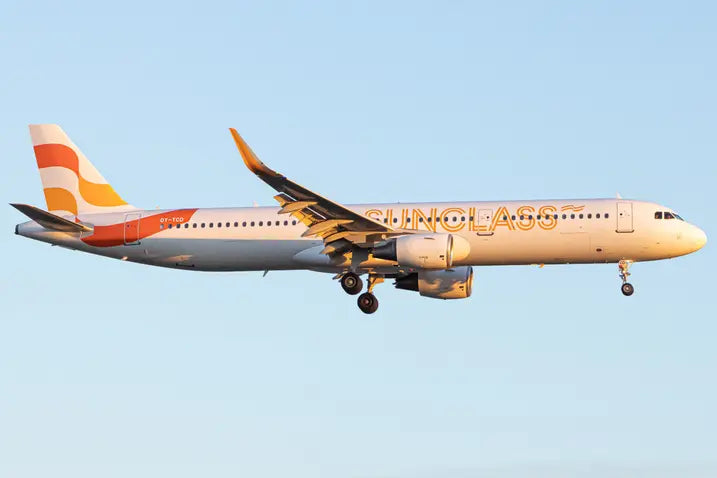 Passenger airplane with 'Sundclass' branding and registration OY-TCD flying in clear sky, side view, with evening sunlight illuminating the aircraft.
