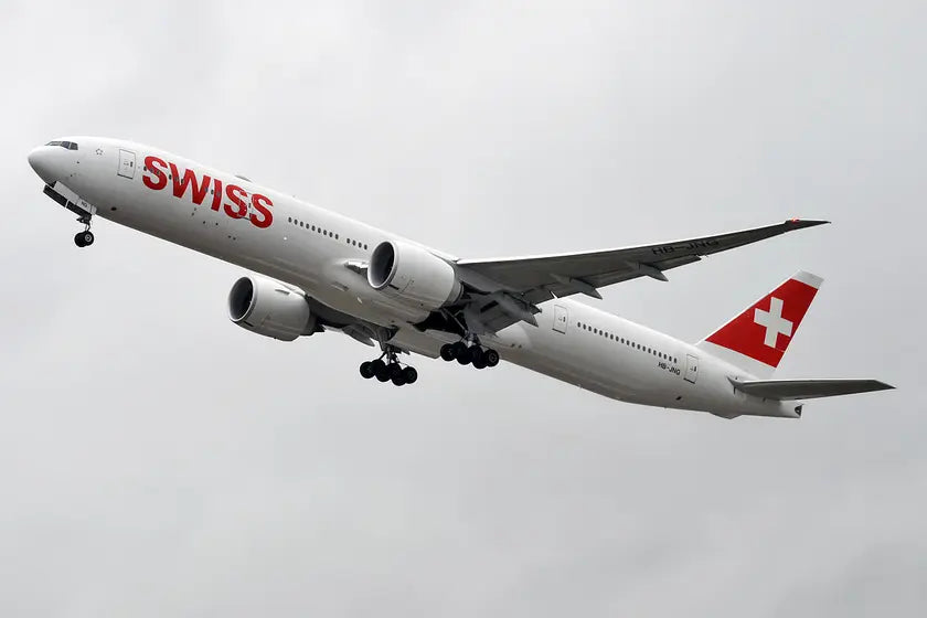Swiss Boeing 777-3DE ER aircraft with registration HB-JNG in flight, showing the Swiss logo and tail emblem against a cloudy sky.
