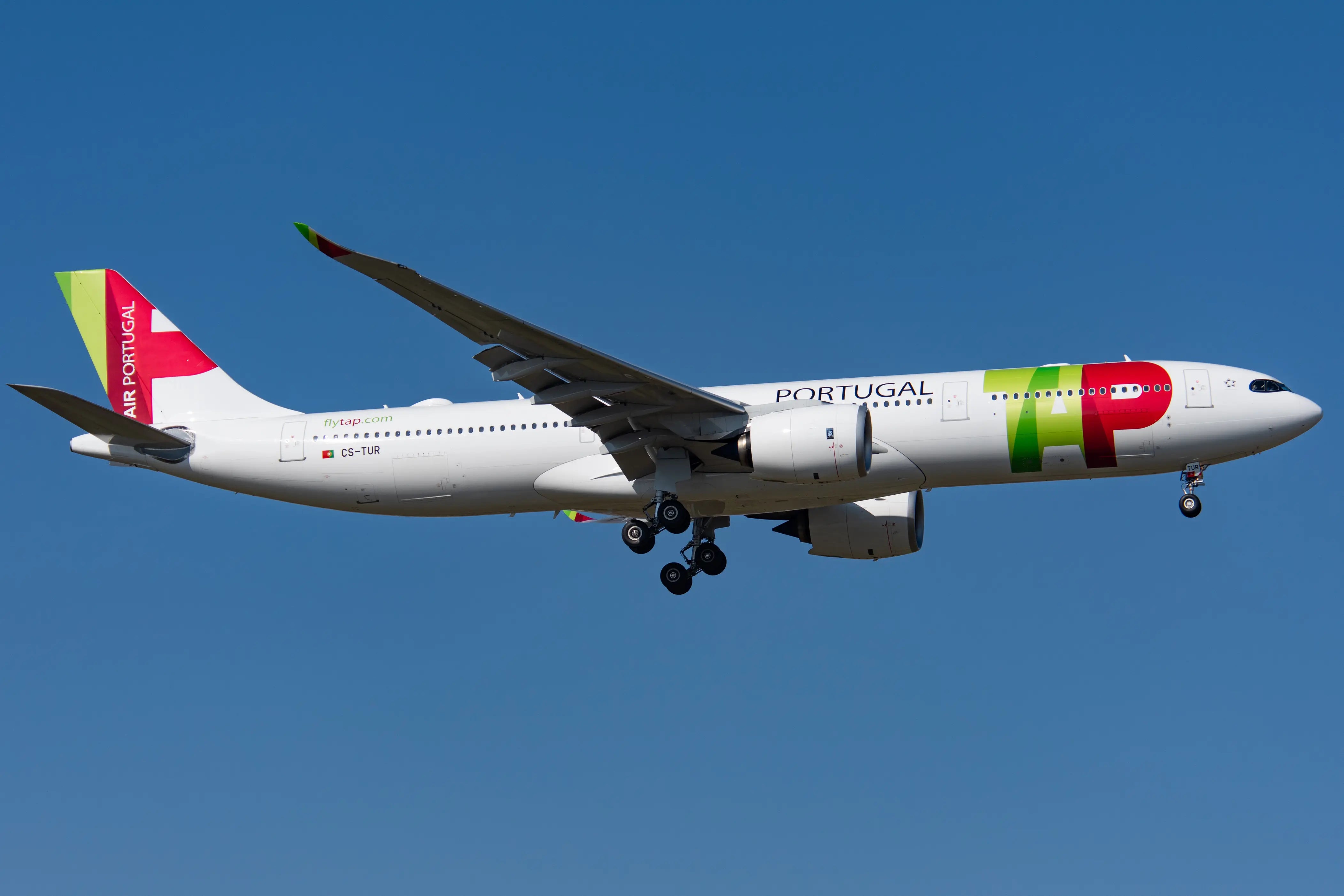 A TAP Air Portugal Airbus A330-900neo in flight with landing gear extended against a clear blue sky.