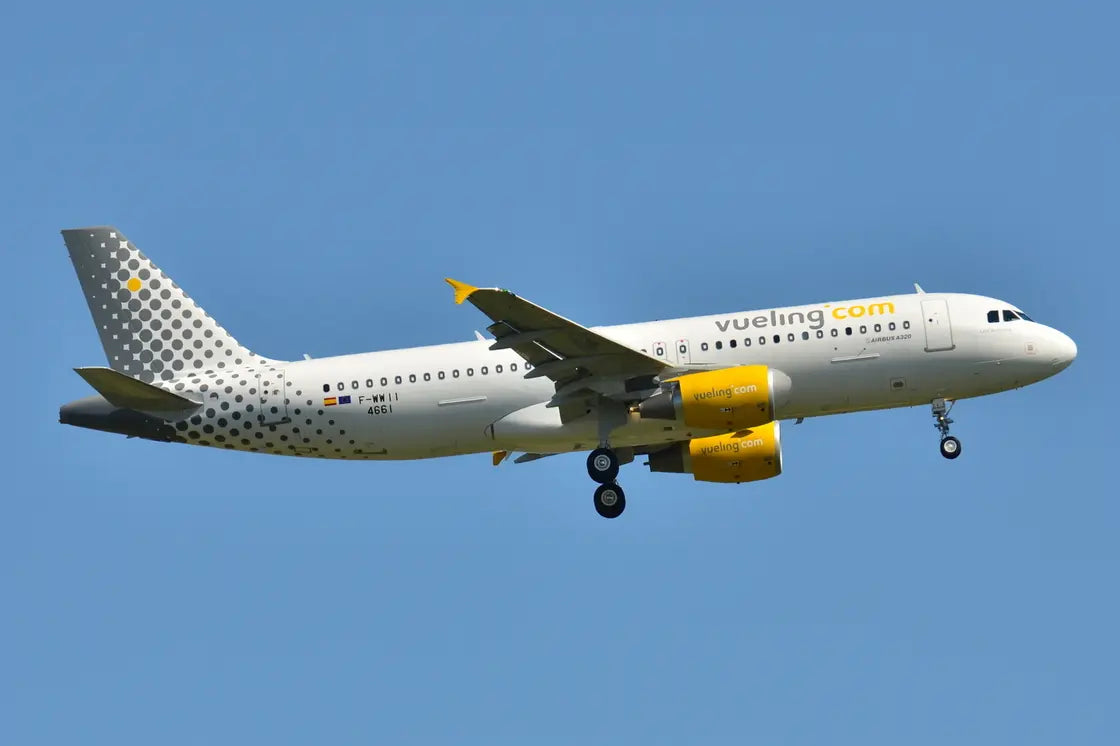 Airbus A320-200 jet with Vueling livery in mid-flight against a clear blue sky.