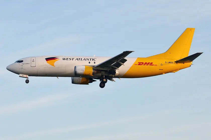 West Atlantic UK Boeing 737-4Q8 SF cargo plane in flight, marked with DHL livery, against a clear sky.